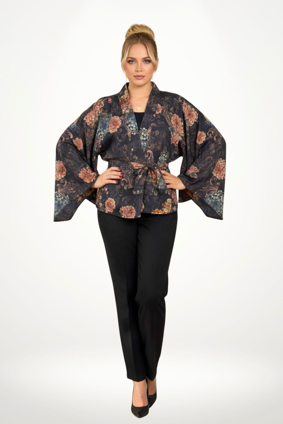 Femme portant un kimono noir à motifs floraux colorés, posant dans un décor sobre avec une lumière douce
