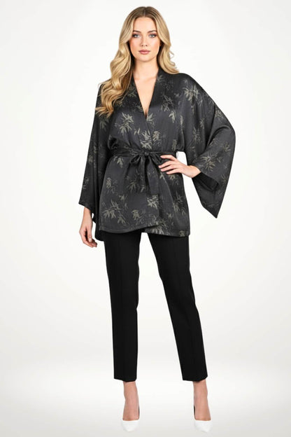Femme en kimono noir à motifs de feuilles, posant dans un décor clair avec des motifs subtils