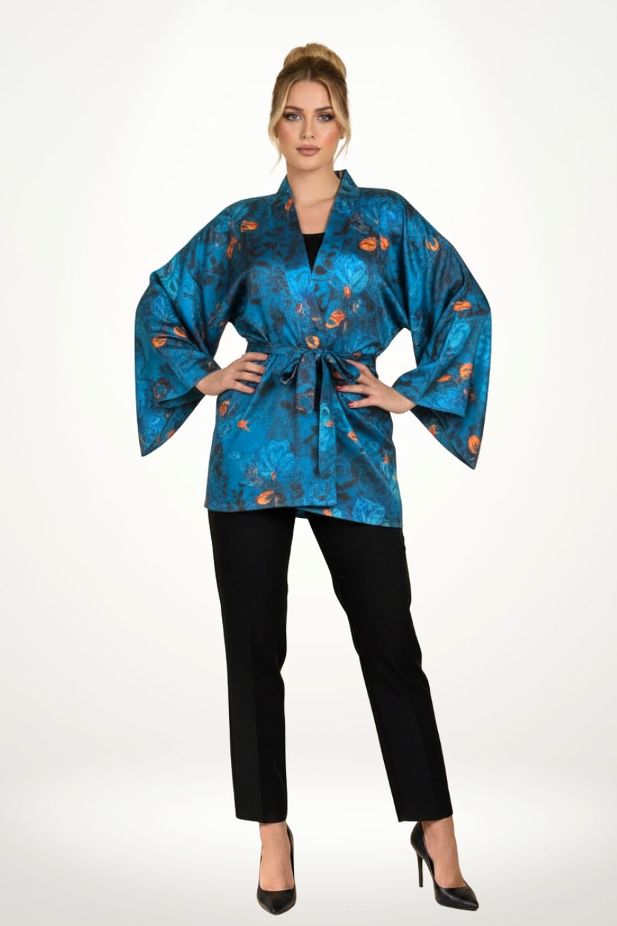 Femme en kimono bleu à motifs floraux orange, posant dans un décor clair et texturé, avec un pantalon noir