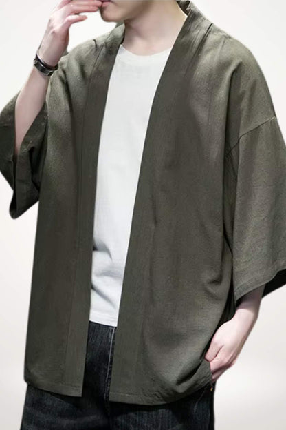 Homme portant un kimono moderne en tissu vert olive, avec un t-shirt blanc et un fond neutre
