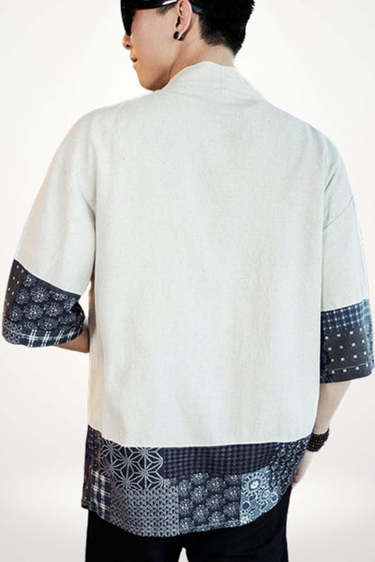 Homme portant un kimono beige avec des motifs bleus sur les manches, dans un décor minimaliste