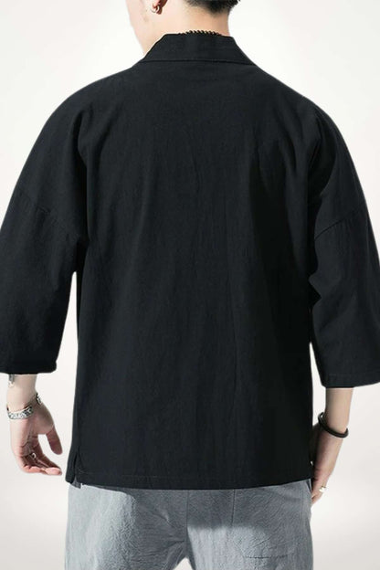 Homme de dos portant un kimono noir à manches larges, avec un fond clair et un décor minimaliste