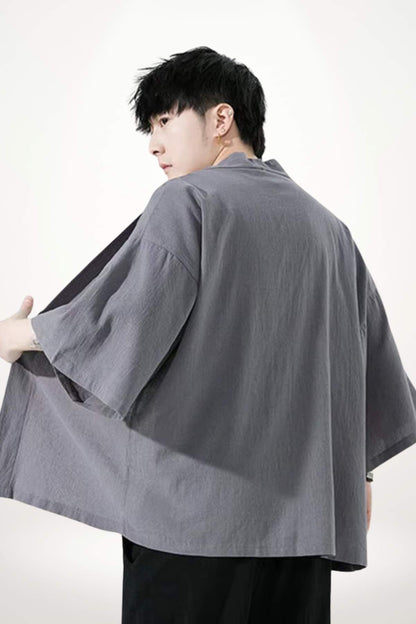 Un homme porte un kimono moderne gris, avec des manches larges, dans un décor minimaliste et lumineux