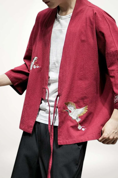 Homme portant un blazer kimono rouge avec des broderies de grues sur un fond neutre