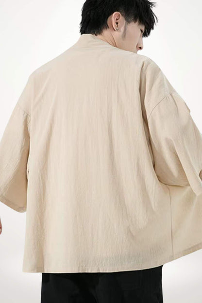 Homme portant un kimono beige, avec des manches larges, se tenant de dos sur un fond neutre