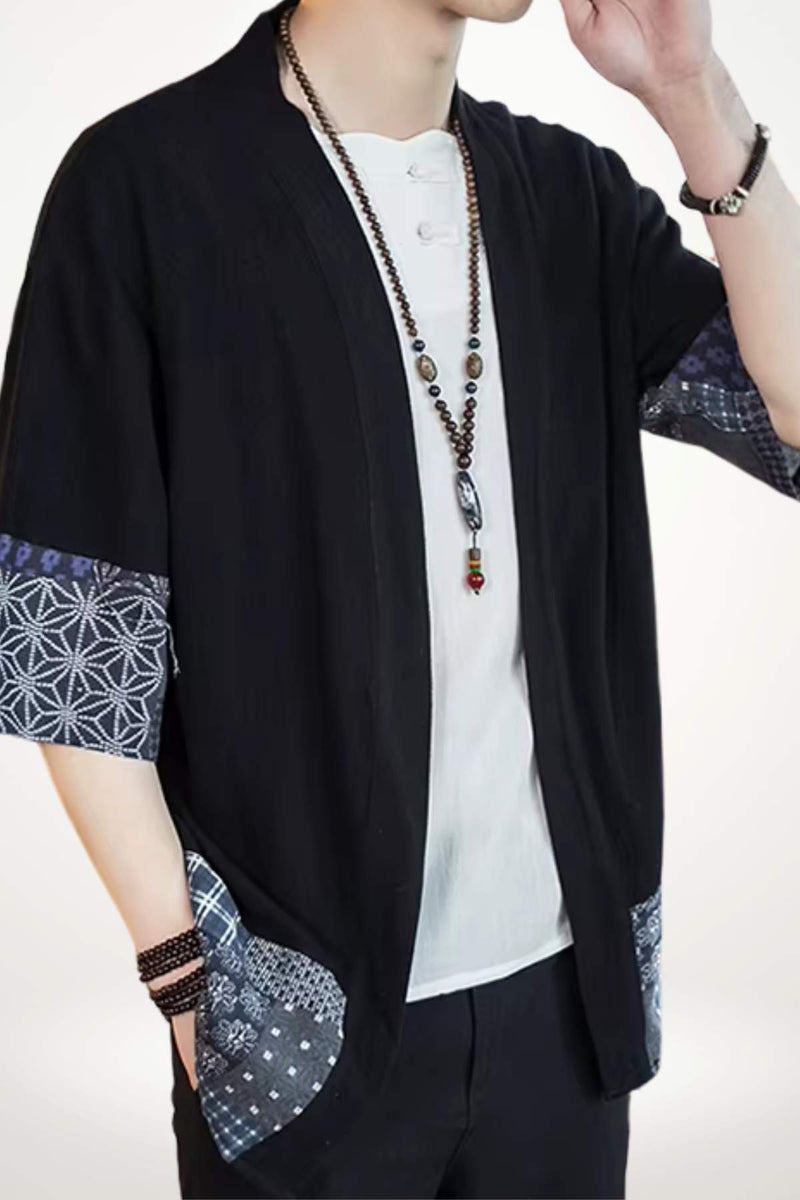 Veste noire style kimono avec manches à motifs géométriques bleus, portée par un homme au décor neutre