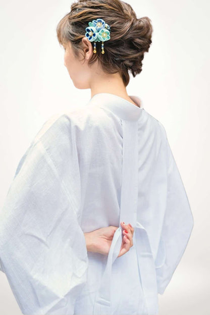 Femme portant un kimono blanc, dos tourné, avec des détails en tissu léger et un accessoire floral coloré dans les