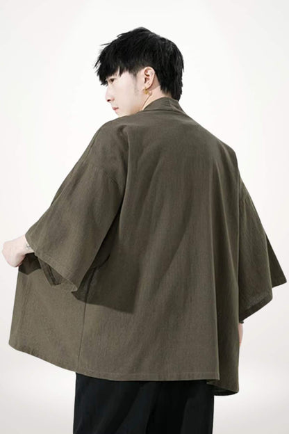 Homme portant un kimono moderne en tissu olive, avec des manches larges, se tenant de dos sur fond neutre