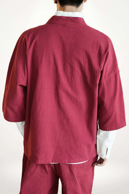Homme de dos portant un kimono moderne rouge, avec des manches larges et un décor minimaliste en arrière-plan
