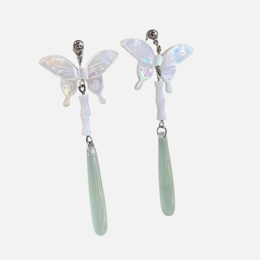 Boucles d'oreilles en forme de papillon, nacrées et légères, avec des pendants en jade vert, sur fond rose.
