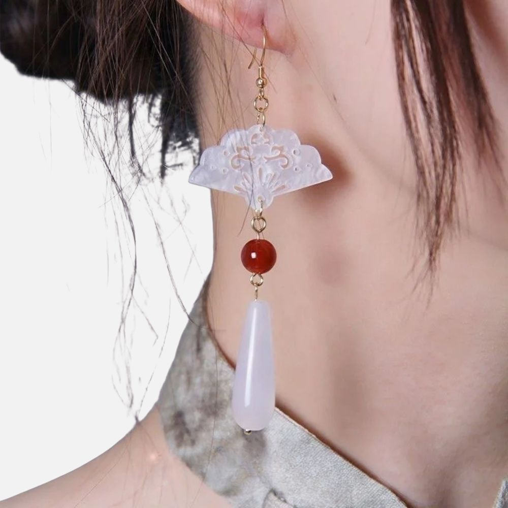 Boucles d'oreilles en forme d'éventail, ornées de perles rouge et blanche, suspendues par des crochets dorés, évoquant un style japonais.
