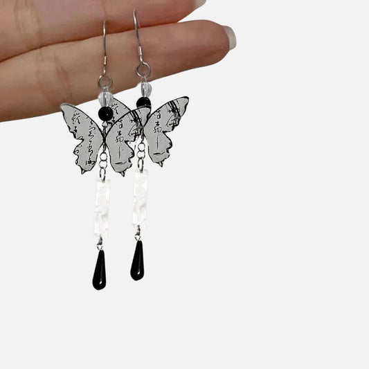 Boucles d'oreilles en forme de papillon avec motifs de calligraphie japonaise, noir et argenté, suspendues à une main