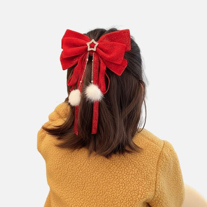 Un nœud rouge scintillant avec des pompons blancs et des rubans, porté sur des cheveux bruns, devant un fond neutre