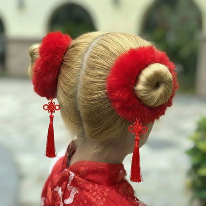 Coiffure en chignons blonds ornée de pompons rouges et de pendentifs, portée avec un kimono rouge