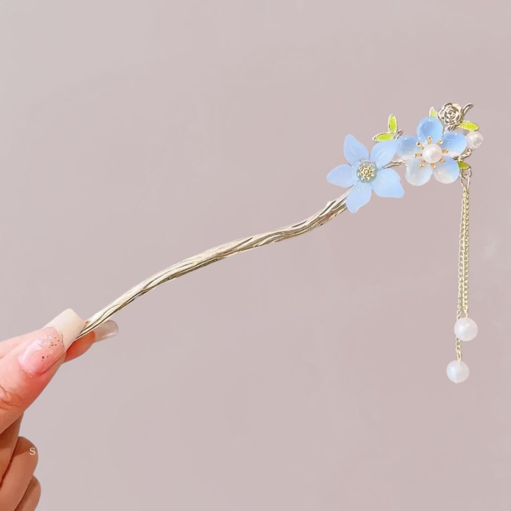 Peigne en métal doré orné de fleurs bleues et perles suspendues, sur fond neutre