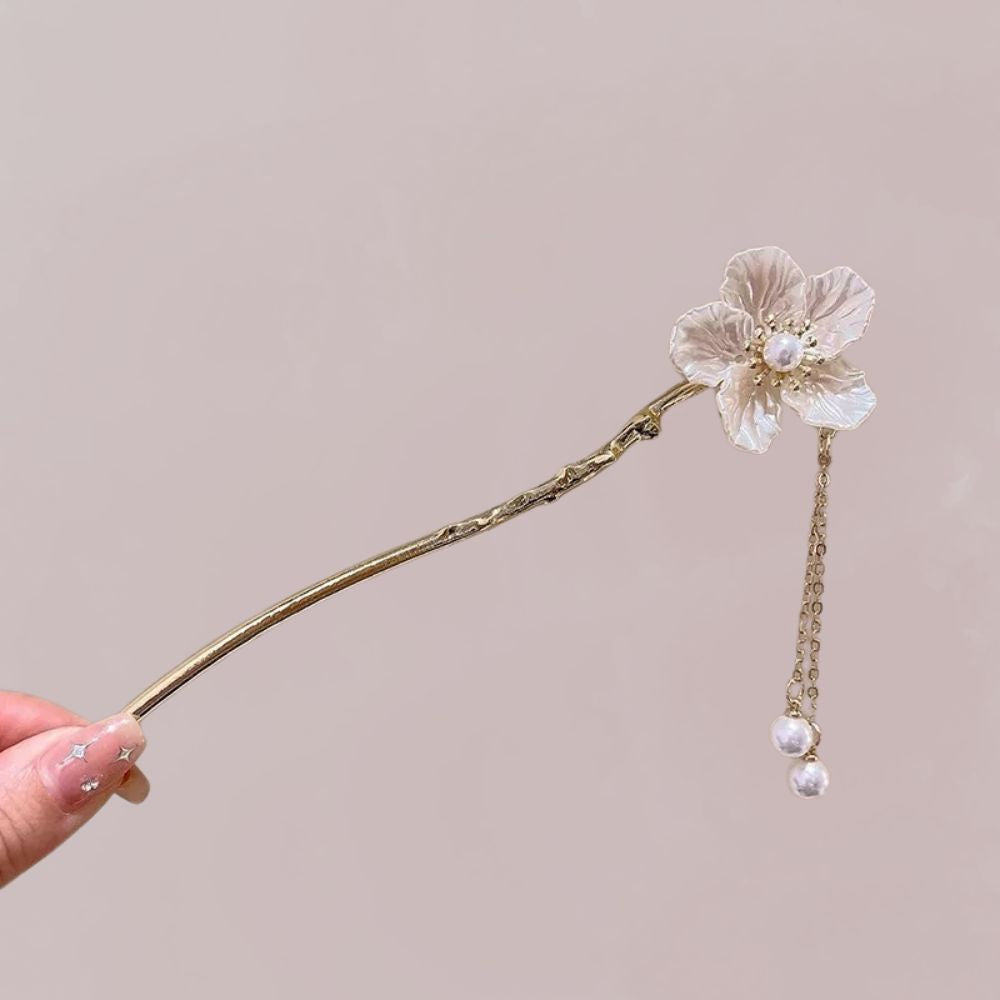 Ornement de cheveux en métal doré avec une fleur ivoire et des perles suspendues, sur fond rose