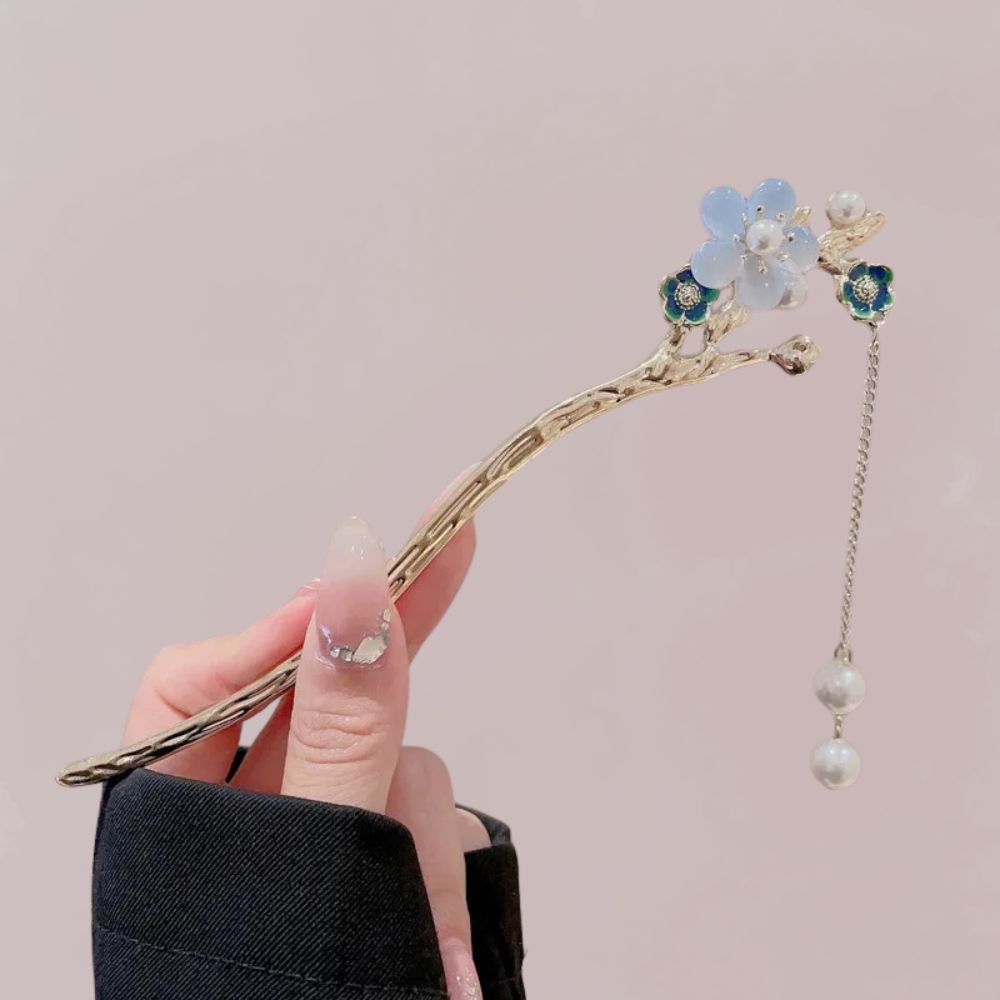 Ornement de cheveux en forme de branche dorée avec fleurs bleues et perles, tenu par une main délicate