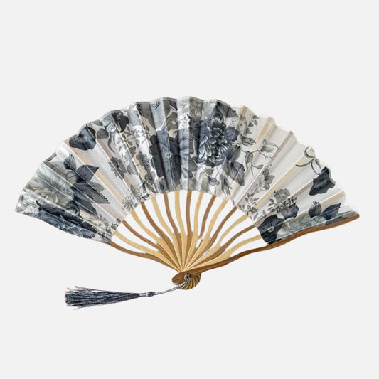 Éventail en papier avec motifs floraux gris et blancs, monture en bois clair et pompon en fil