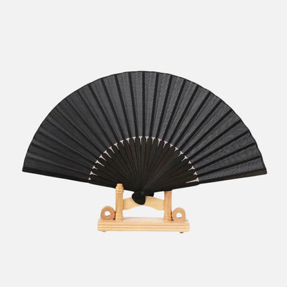 Éventail noir en papier, avec des lames en bois, posé sur un support en bois clair