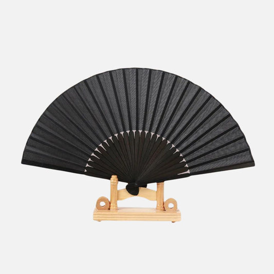 Éventail noir en papier, avec des lames en bois, posé sur un support en bois clair
