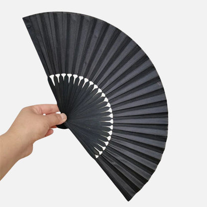 Un éventail noir en papier est tenu à la main, avec des plis bien marqués et une texture lisse