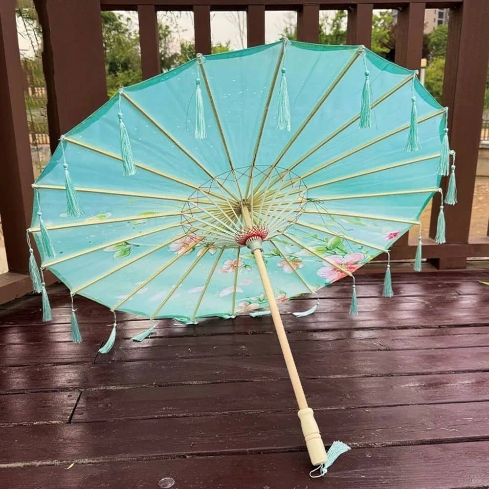 Parapluie japonais bleu avec des motifs floraux, décoré de franges et posé sur un sol en bois