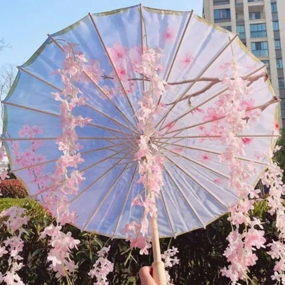 Parapluie japonais en papier bleu orné de fleurs roses et de branches, tenu devant un fond verdoyant