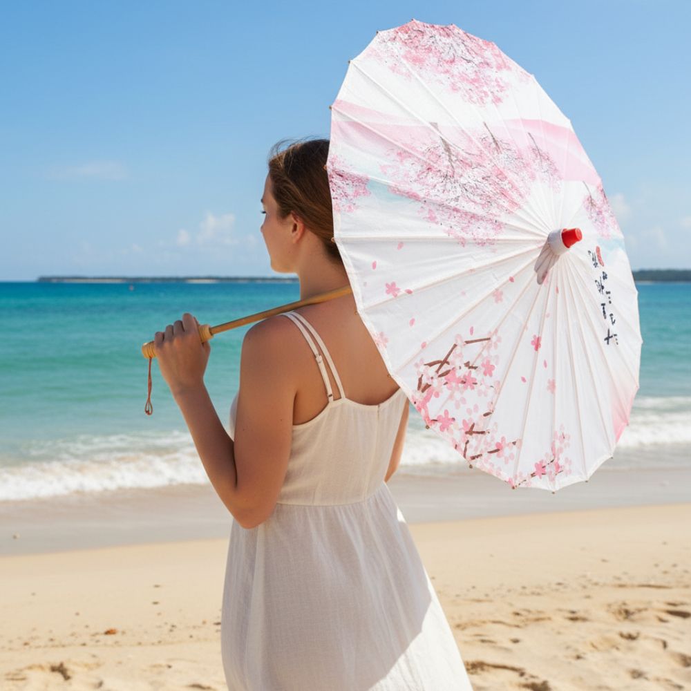 Femme en robe blanche tenant une ombrelle blanche ornée de fleurs roses sur une plage ensoleillée