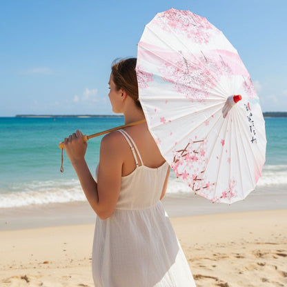 Femme en robe blanche tenant une ombrelle blanche ornée de fleurs roses sur une plage ensoleillée