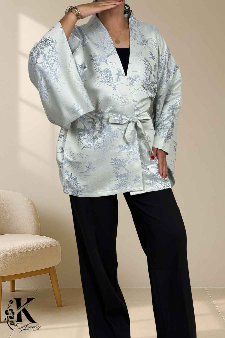 Femme portant un kimono gris clair avec motifs floraux bleus, associé à un pantalon noir, en pose élégante