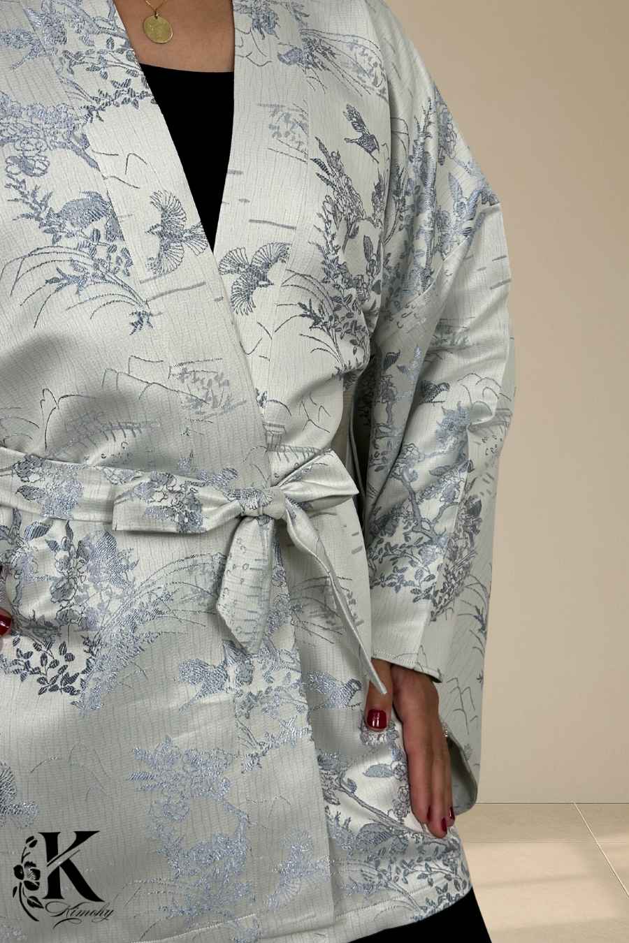 Kimono en satin clair avec motifs floraux et oiseaux, ceinturé à la taille, porté sur un fond texturé