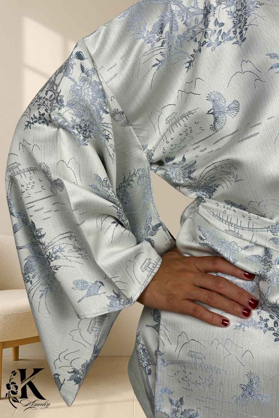 Kimono féminin en satin blanc avec motifs floraux et oiseaux bleus, porté avec une main sur la taille