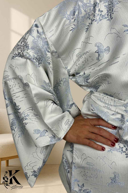 Kimono féminin en satin blanc avec motifs floraux et oiseaux bleus, porté avec une main sur la taille