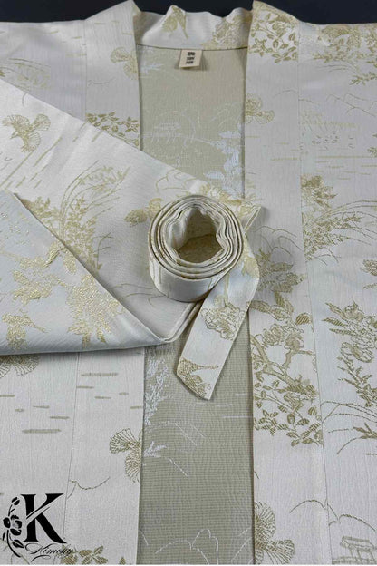 Kimono élégant en soie blanche avec motifs dorés représentant des fleurs et des paysages japonais, délicatement plié