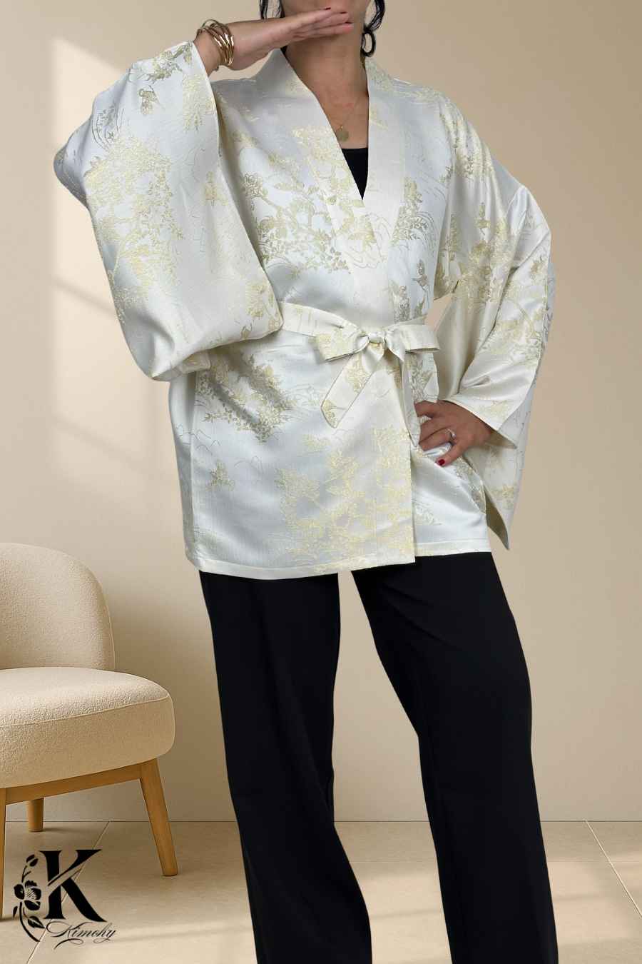 Femme portant un kimono blanc avec des motifs dorés, ceinturé, sur un fond décoratif clair et texturé