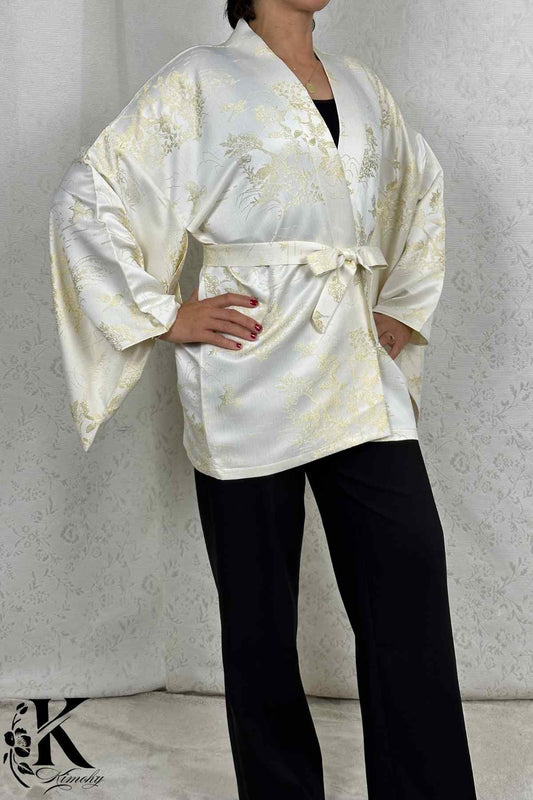 Femme portant un kimono blanc satiné avec motifs dorés, ceinturé, sur fond décoratif clair