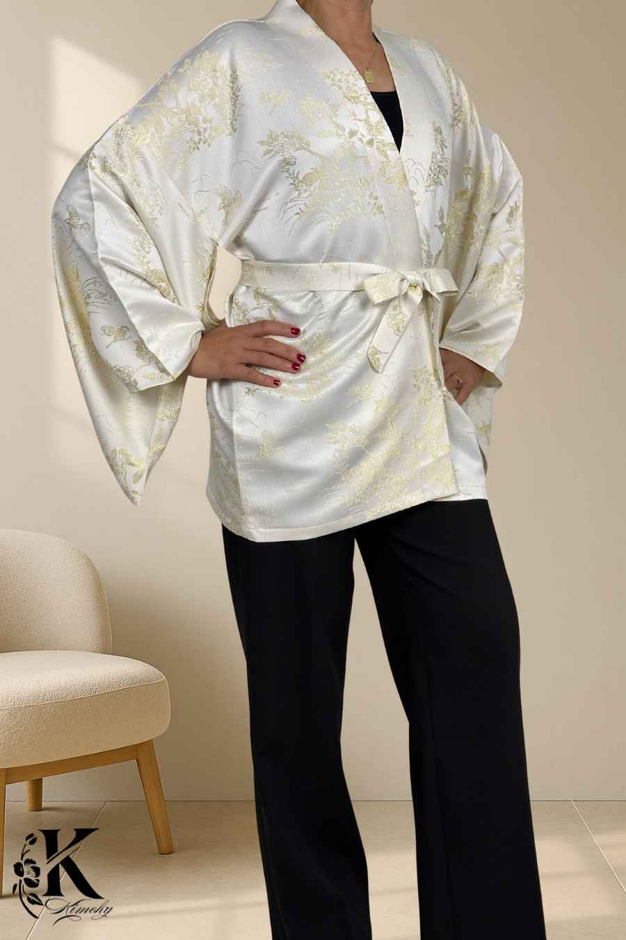 Femme portant un kimono blanc satiné avec motifs dorés, ceinturé, sur fond décoratif clair