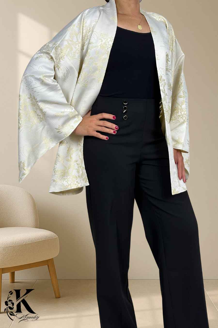 Femme portant un kimono blanc à motifs dorés, avec un pantalon noir, dans un décor sobre et élégant