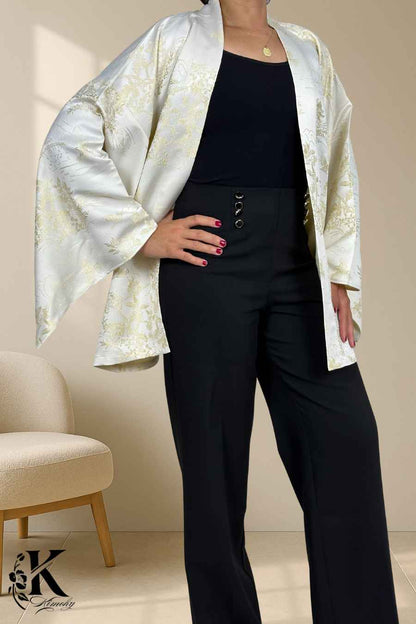 Femme portant un kimono blanc à motifs dorés, avec un pantalon noir, dans un décor sobre et élégant