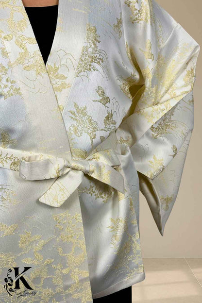 Kimono chic en satin blanc avec motifs dorés, noué à la taille, sur fond texturé clair