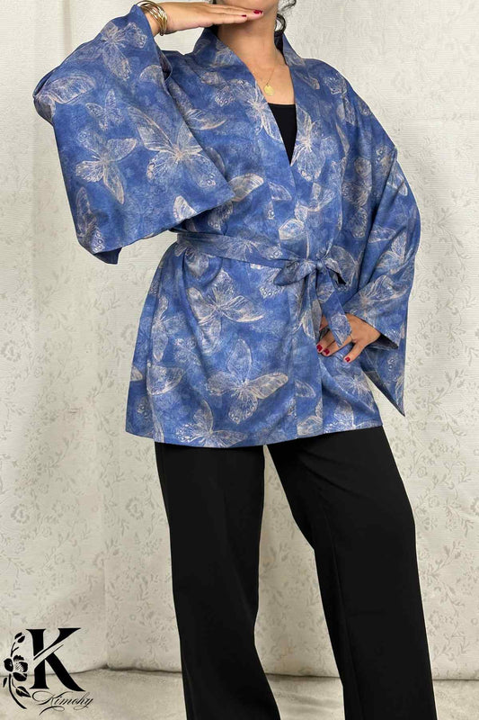 Kimono bleu avec motifs de papillons, manches larges, porté avec un pantalon noir sur fond clair