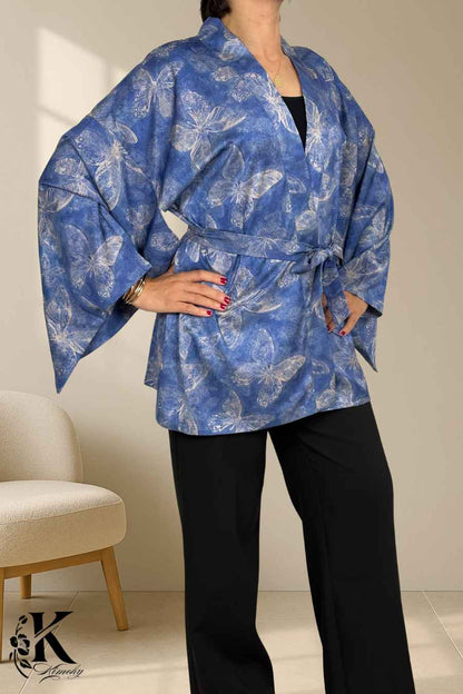 Femme portant un kimono bleu à motifs de papillons, avec des manches larges et un pantalon noir, sur fond clair