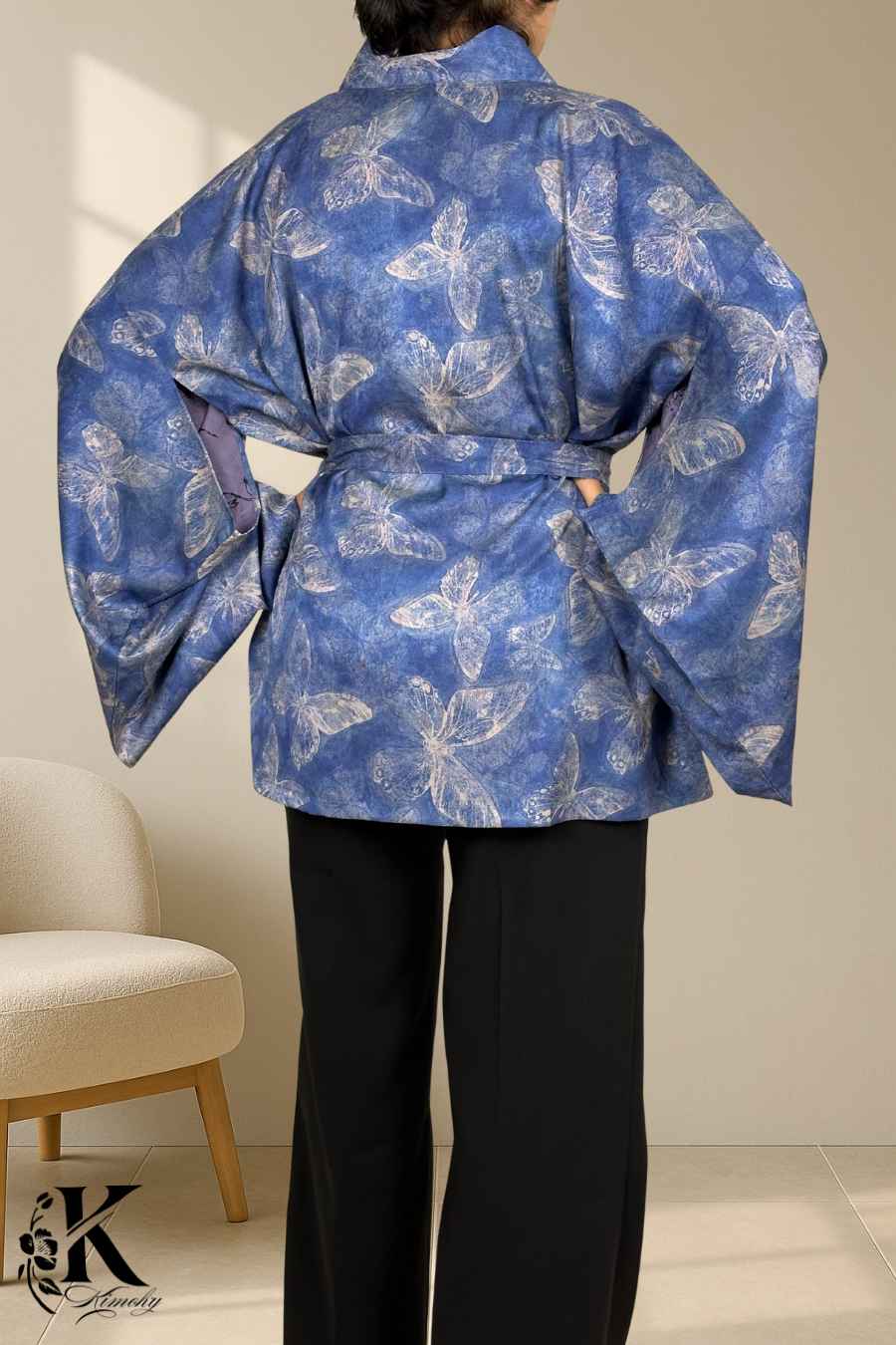 Kimono bleu avec motifs de papillons, manches larges, ceinture nouée, porté avec un pantalon noir, fond clair