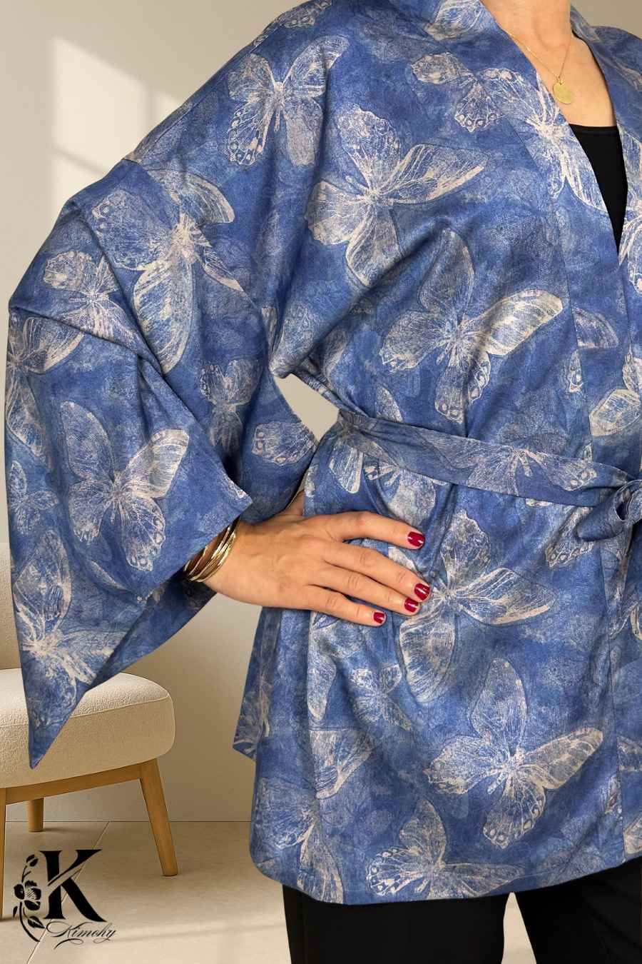 Kimono bleu avec motifs de papillons, manches larges, porté avec un pantalon noir, décor sobre en arrière-plan