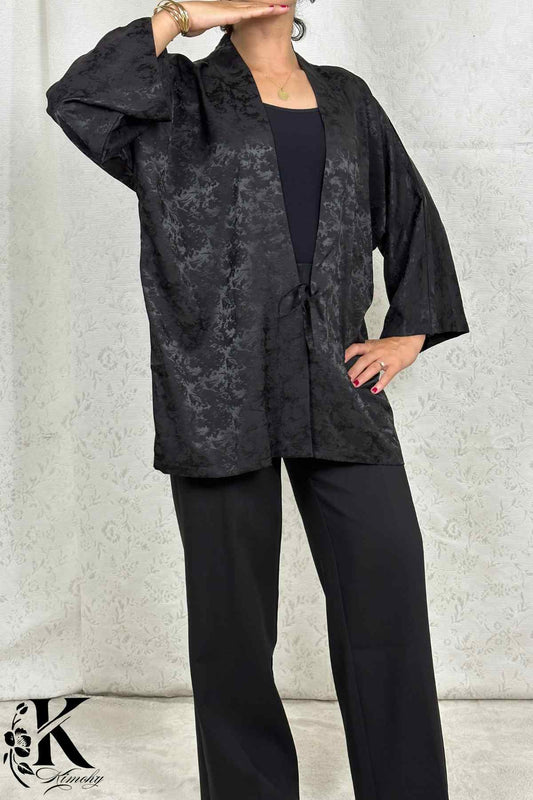 Femme portant un kimono noir à motifs délicats, posé sur un fond clair avec des détails floraux
