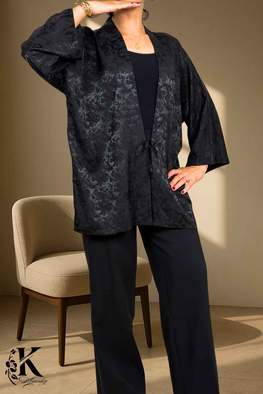 Femme portant un kimono noir à motifs délicats, posé sur un fond clair avec des détails floraux
