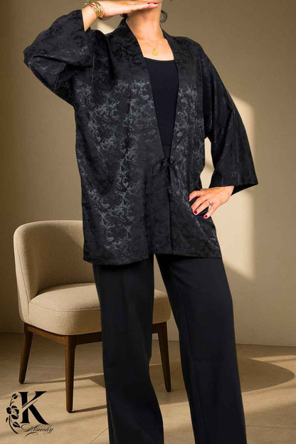 Femme portant un kimono noir à motifs délicats, posé sur un fond clair avec des détails floraux