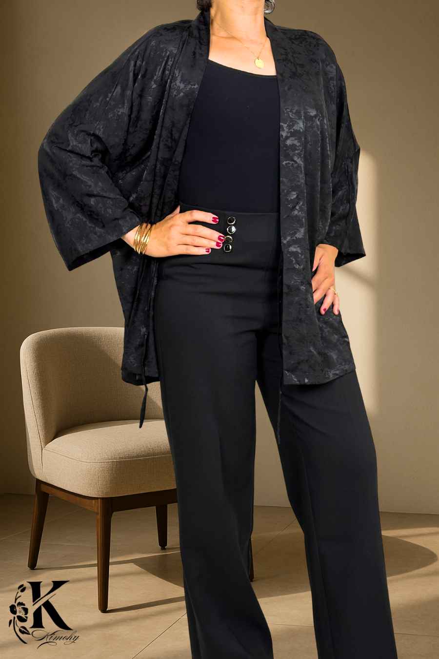 Femme en kimono noir avec motifs subtils, posant avec élégance sur fond clair et décor floral