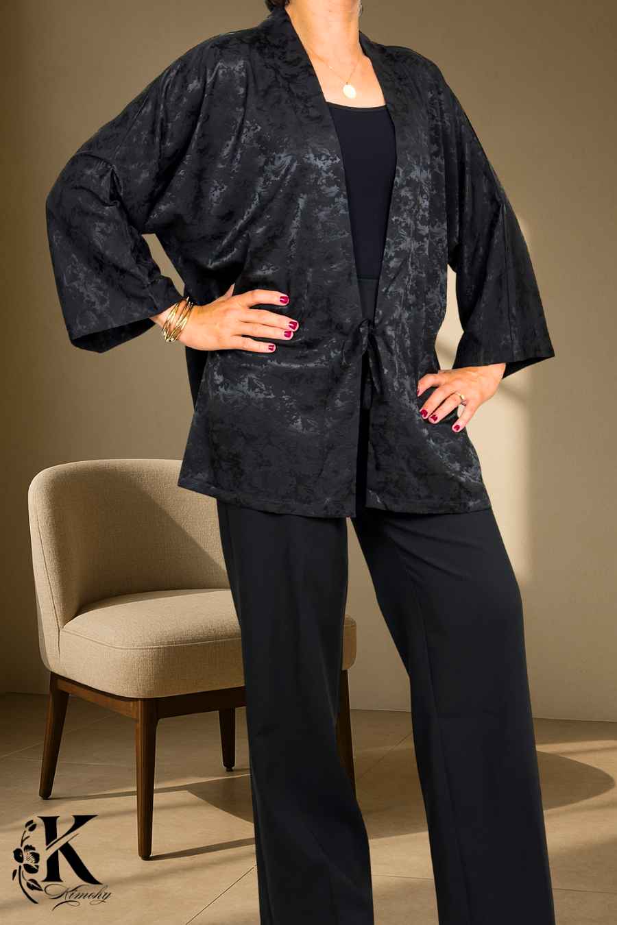Femme en kimono noir avec motifs subtils, posant dans un décor clair et élégant, portant un pantalon noir