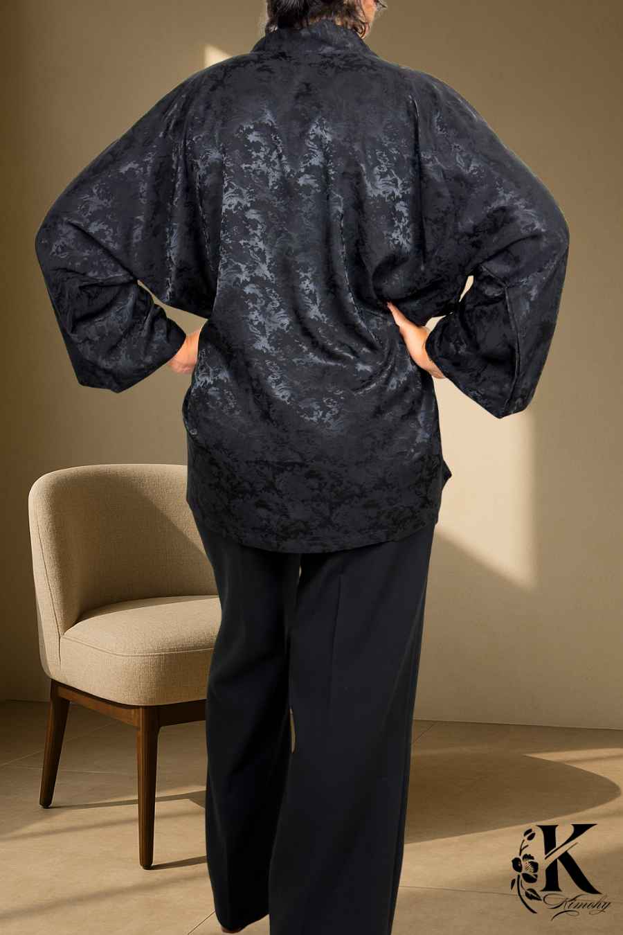 Femme de dos portant un kimono noir à motifs, avec un fond de tissu clair et texturé